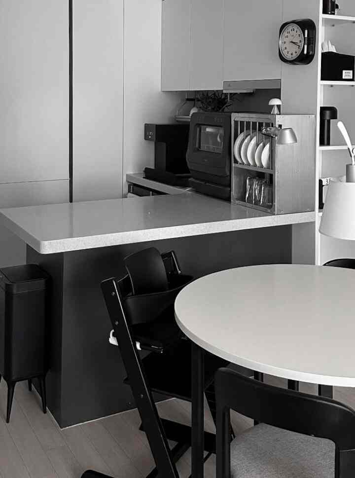 モノトーンのキッチン空間、白い円形のダイニングテーブルと黒いダイニングチェアが配置された清潔感のあるモダンなインテリア