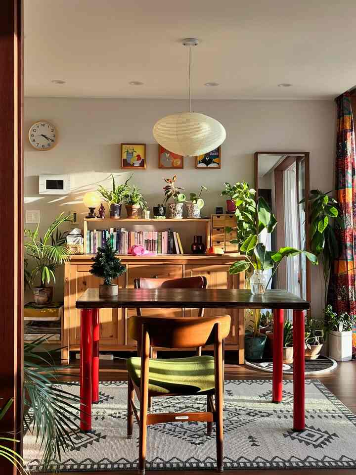 自然な木目調と赤のアクセントが調和したリビング、ダイニングテーブルと椅子、植物が配置された温かみのある空間