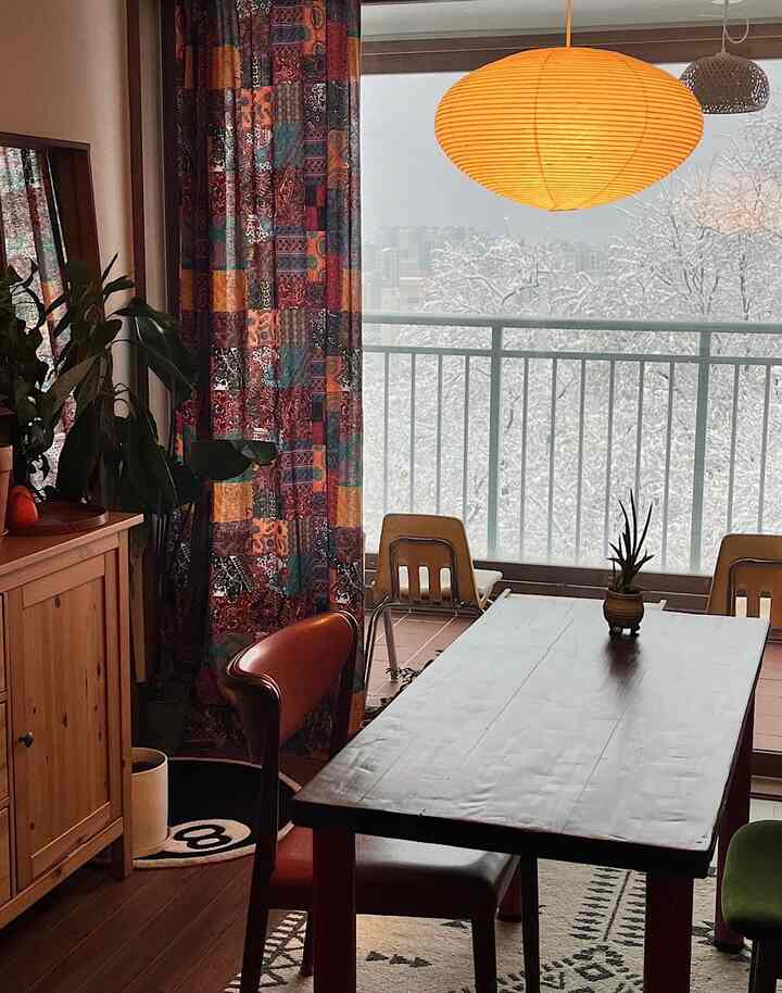 ブラウンと木目調のダイニングルーム、柄のあるカーテンと植物が自然な雰囲気を演出する冬の景色が見える空間