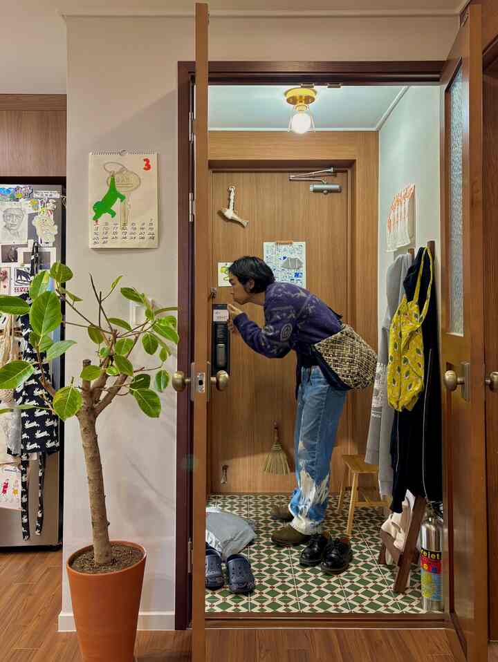 木目調の壁と床タイルがある狭い玄関、大きな植物とコートハンガーが配置された温かみのある雰囲気のインテリア