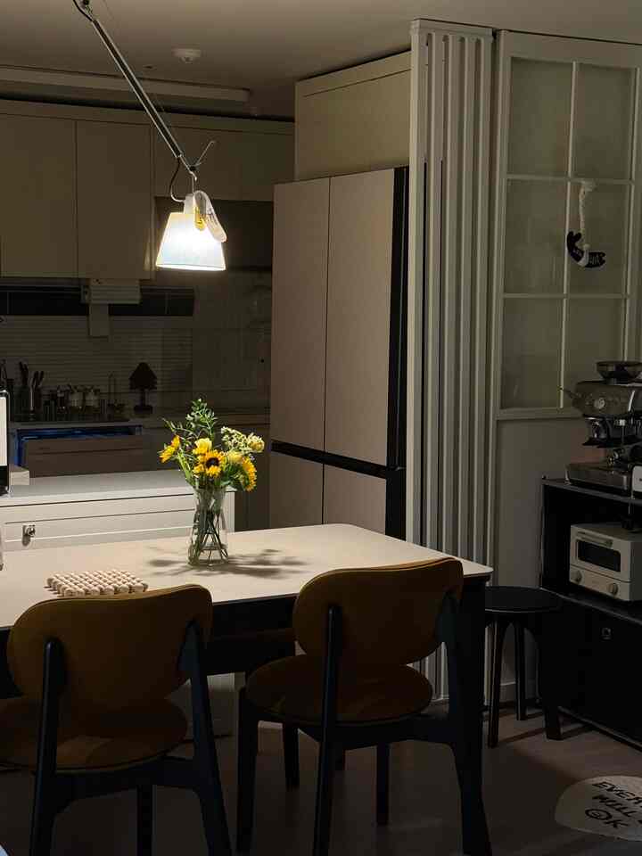 白と茶色のトーンのキッチンスペース、アルテミデの壁照明が柔らかな光を放ち、温かみのあるおうちカフェの雰囲気を演出する空間