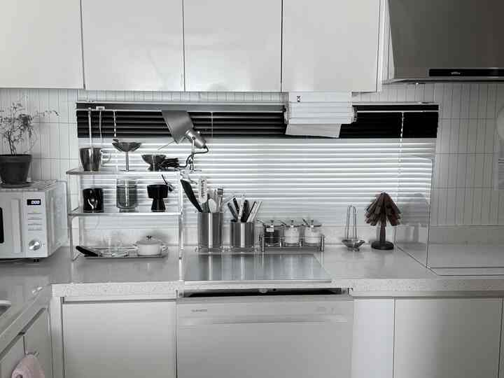 ホワイトとシルバーのモダンなキッチン、黒と白のツートーンブラインドとステンレスのまな板が整然と配置された雰囲気のあるインテリア