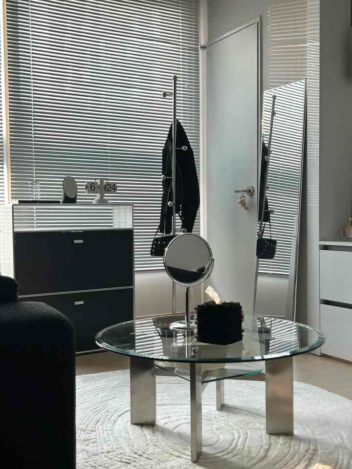 ブラックとシルバーのトーンが調和したモダンなリビングルーム、ガラスのコーヒーテーブルとブラインド、そして全身鏡が配置された印象的な空間