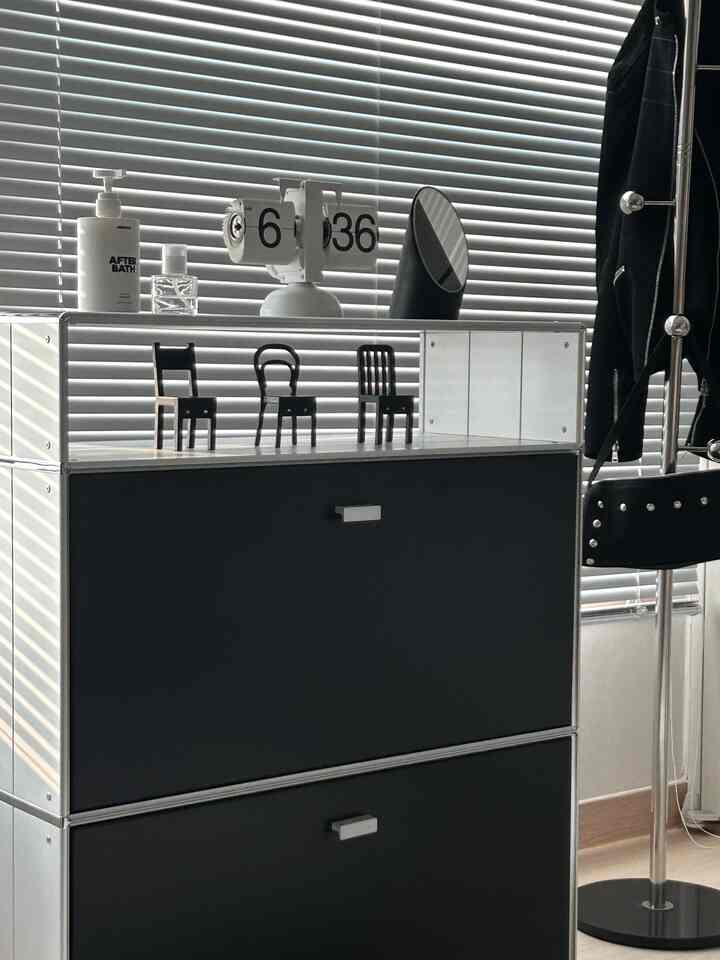 シルバーと黒のトーンのリビングにブラインドと収納家具が配置されたミニマルなインテリア