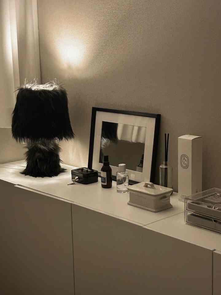 暖かいベージュとホワイトトーンの収納棚が配置されたミニマルな空間、黒いファーのテーブルランプと額縁が雰囲気を演出