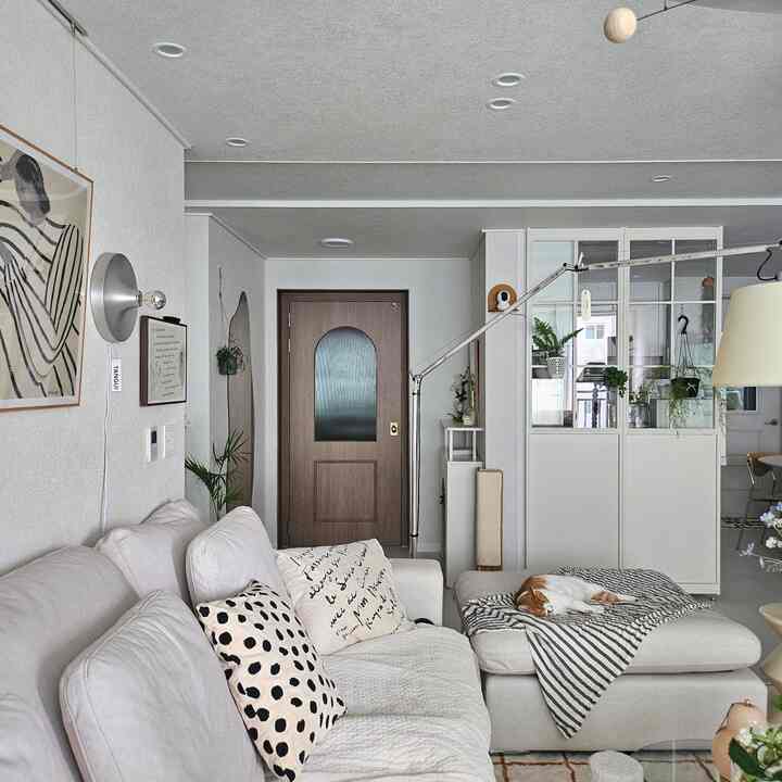 ナチュラルモダンのリビングルーム、ベージュのソファとクッション、木目調のドア、くつろぐ猫がいる温かみのある空間