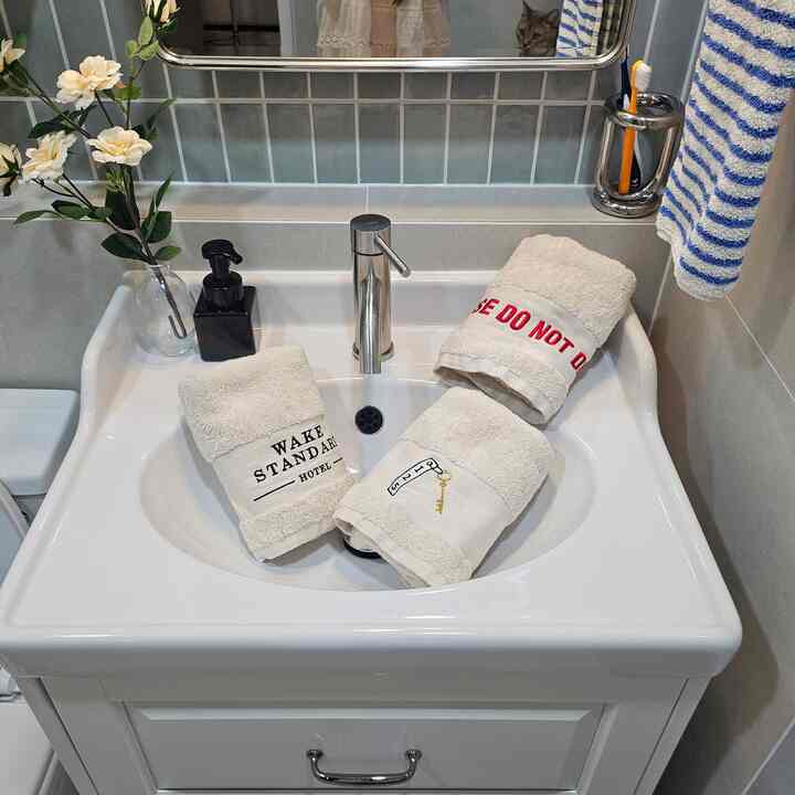 ホワイトとグレーのトーンのバスルーム、イケアの洗面台とタオル、歯ブラシホルダー、造花が配置された清潔で居心地の良いインテリア