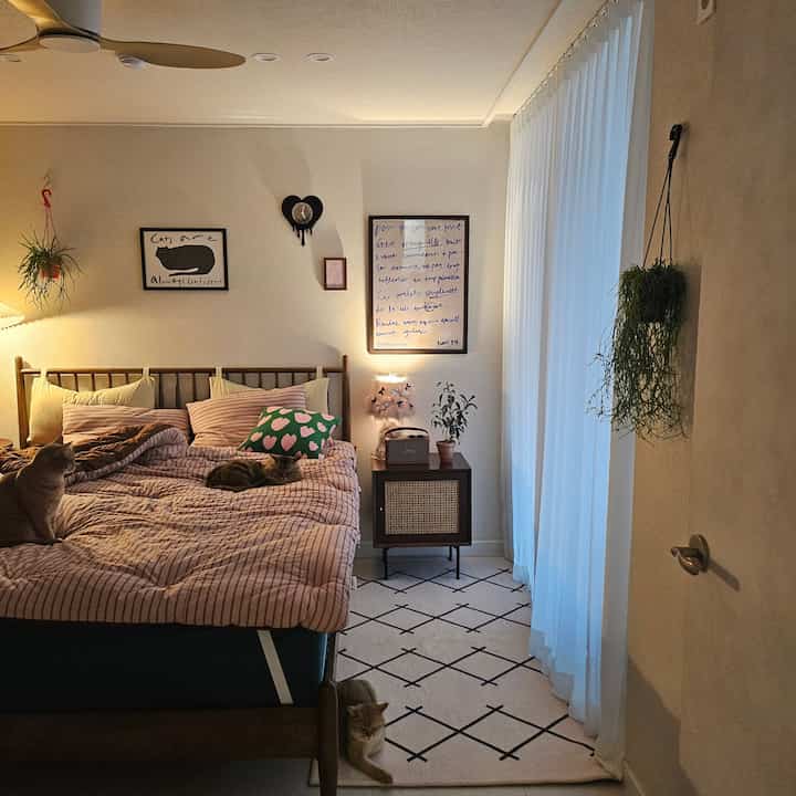 ナチュラルな色調の寝室、木製ベッドフレームとストライプの寝具、壁にポスターと時計が配置された雰囲気のあるインテリア