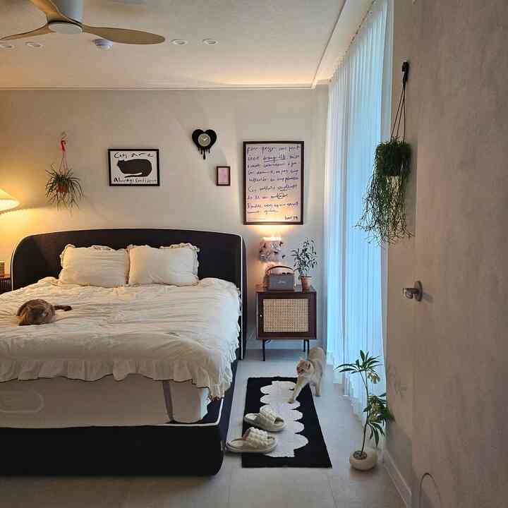 クリーム色の寝具と黒いファブリックのベッドフレームが配置された寝室、二匹の猫がいるナチュラルで落ち着いた雰囲気のインテリア