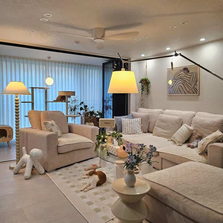 ベージュ調のリビング、コーナーソファとアームチェア、キャットタワーとペットの猫がいる温かみのある空間