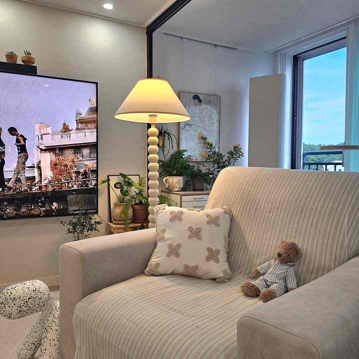 ベージュとナチュラルカラーの調和したリビングルーム、ソファとフロアランプ、多数の植物が落ち着いた雰囲気を演出する空間