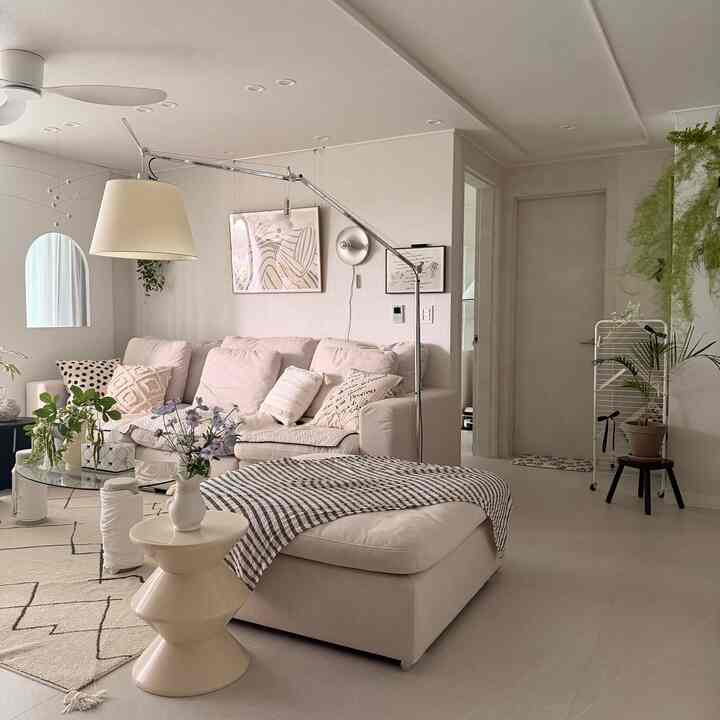 明るいベージュトーンのリビング、広いソファとフロアランプ、クッションや植物が配置された居心地の良い空間