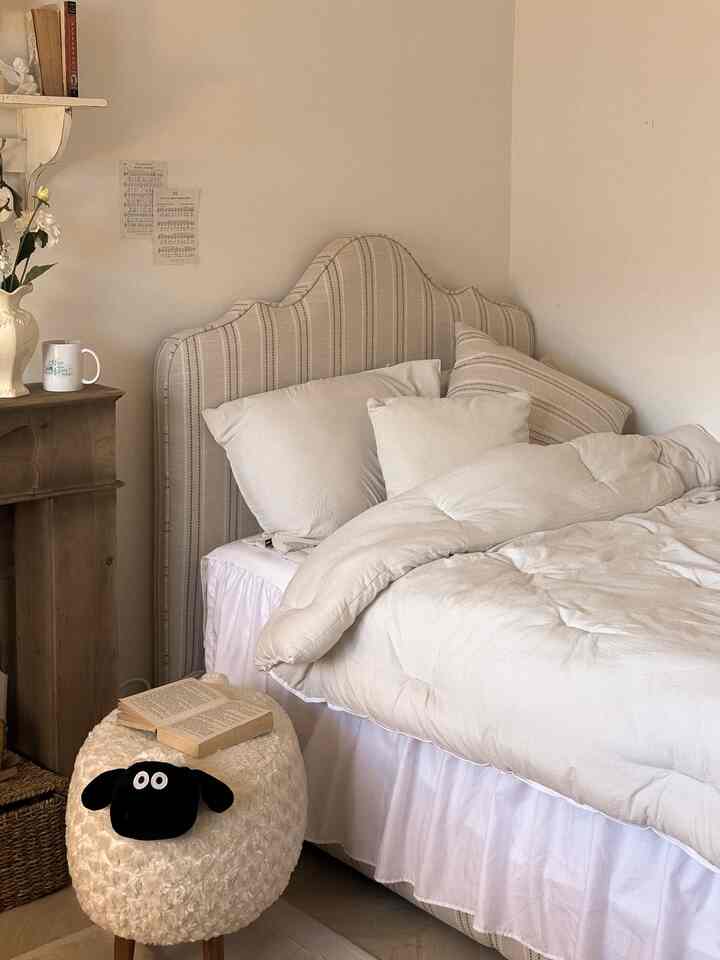 柔らかなベージュとホワイトのトーンの寝室、ストライプのファブリックベッドとアンティークの木製チェストが配置された雰囲気のあるインテリア