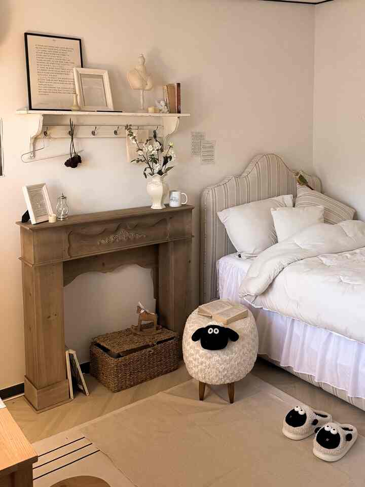 アイボリーの色調の寝室、暖炉風コンソールと羊形のスツール、快適な寝具が配置されたフレンチカントリースタイルのインテリア