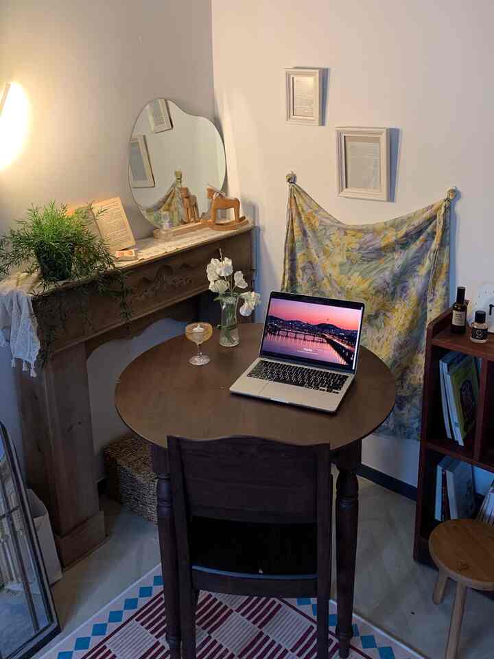 ナチュラルな木目調のダイニング、丸い木製テーブルと椅子、壁に額縁と布の装飾が配置された暖かく居心地の良い空間