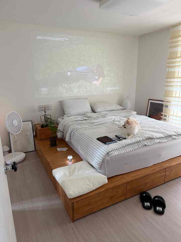 白とブラウンの木目調の寝室、大型の木製収納付きベッドフレームと快適な寝具が配置されたシンプルモダンなインテリア