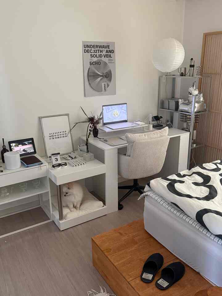 白と木目調が調和した一人暮らしの寝室兼ホームオフィス、クッションの上に小さな犬が座っている様子