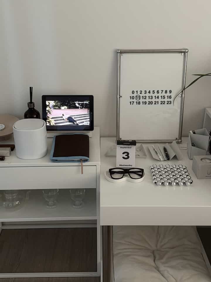 白を基調としたホームオフィス空間、ドレッサーとナイトテーブルに文房具とデジタル機器が整然と配置されたミニマルなインテリア