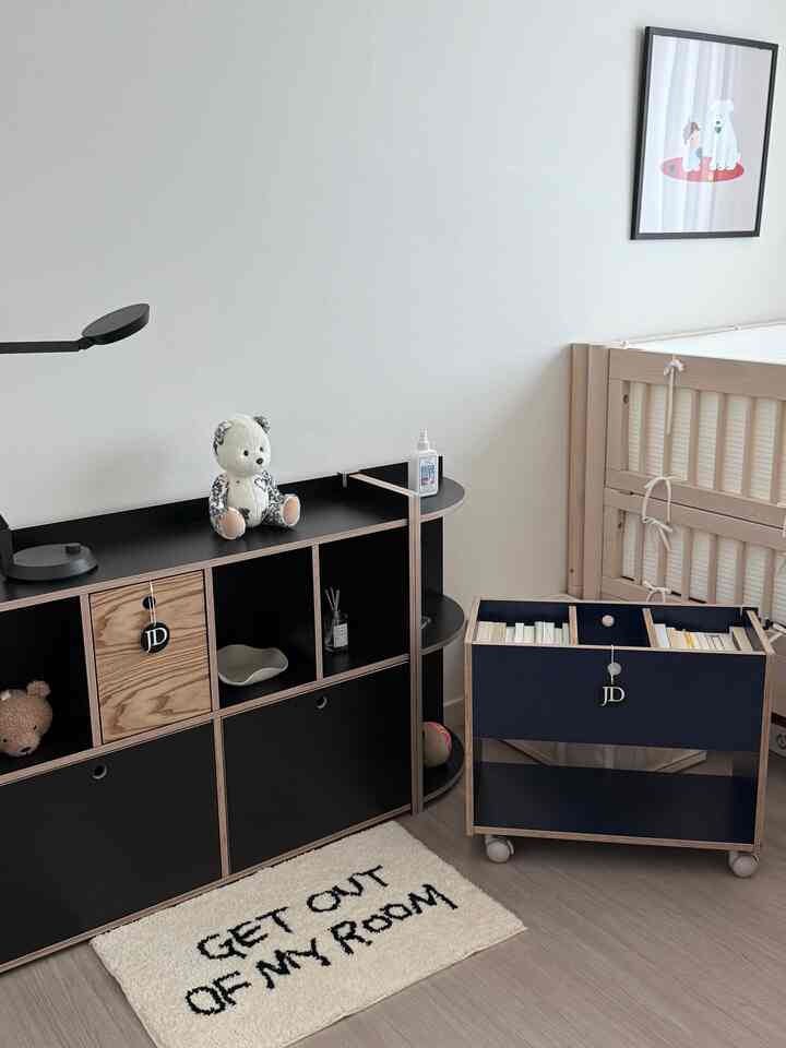 黒と木目調が調和したベビールーム、木製ベビーベッドとマルチ収納家具が配置された落ち着いた雰囲気の空間