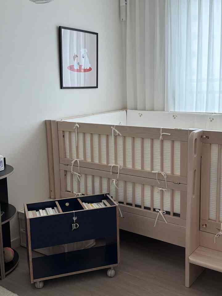 明るいナチュラルカラーとシンプルなデザインの子供部屋、ベビーベッドとネイビーの本棚が配置された雰囲気のある空間