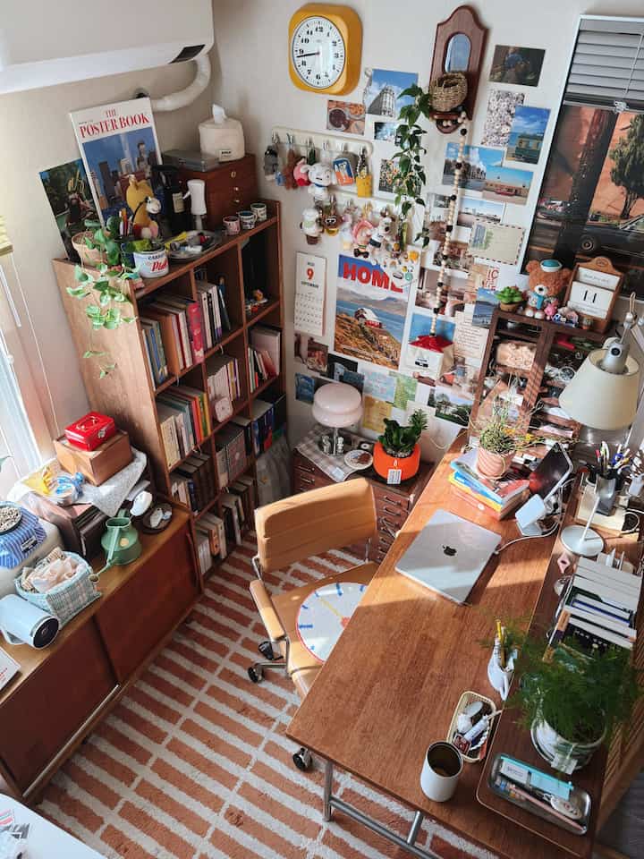 ナチュラルな木目調とイエローの時計が印象的なホームオフィス書斎、書棚と机が配置されたコンパクトな部屋の雰囲気のあるインテリア