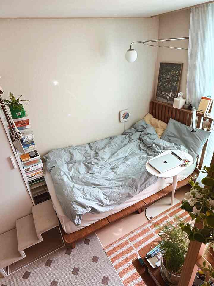 白い壁と木目調家具が調和する一人暮らし用のコンパクトな寝室、書棚と犬用のペットステップがあるナチュラルでシンプルな空間