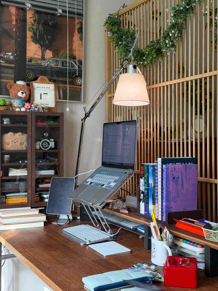 ナチュラルなウッドトーンとベージュの書斎空間、大きな木製デスクにノートパソコン、照明、ガーランドが配置された雰囲気のある作業環境