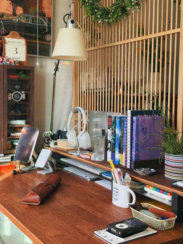 木目調と茶色が調和したホームオフィス空間、モニター台や本棚、フロアランプと植物が配置された温かな作業空間