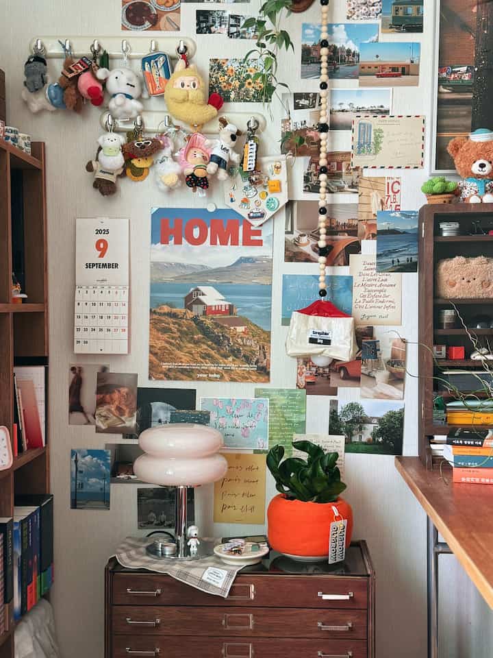 ヴィンテージのポスターとポストカードが飾られた壁、ブラウンの木製家具とオレンジ色の植物鉢が配置された雰囲気のある書斎