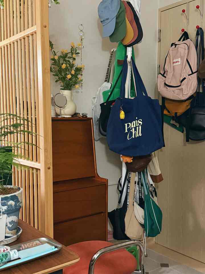 ブラウンとナチュラルカラーの狭い部屋、木製の化粧台と天井まで届くポールハンガーにバッグや帽子が掛けられた雰囲気のあるインテリア