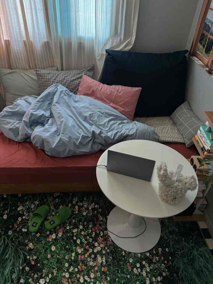 ベージュとネイビーカラーの落ち着いた一人暮らしのリビング、花柄のラグと白い丸テーブルが配置された雰囲気のある空間