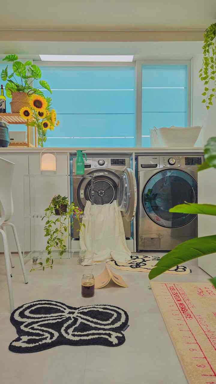 白とシルバーの色調のランドリールーム、洗濯機と乾燥機が並び、棚やひまわりがアクセントとなった落ち着いたインテリア