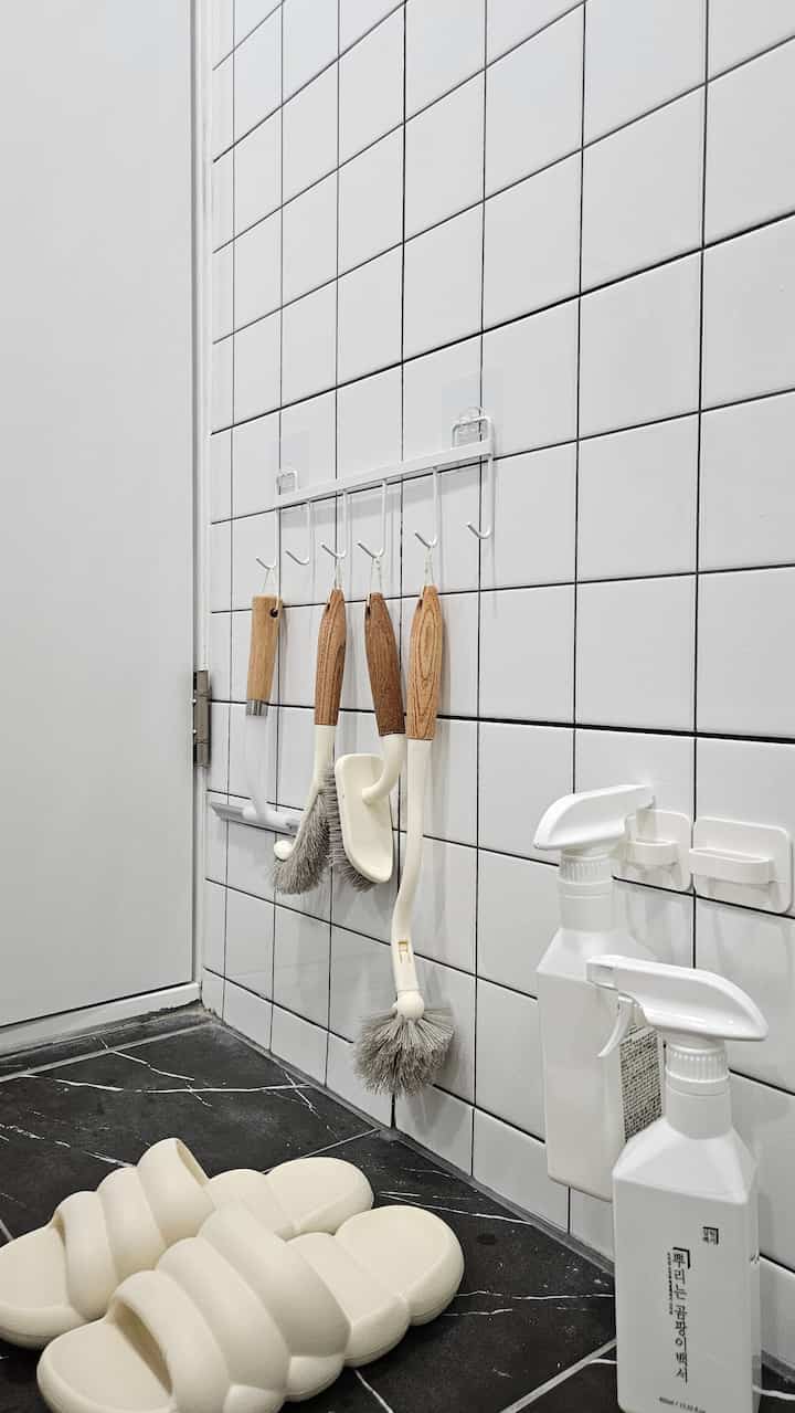 黒い大理石の床と白いタイル壁のあるウォークインクローゼット、木製の掃除用具とアイボリーのスリッパが整頓された雰囲気のあるインテリア