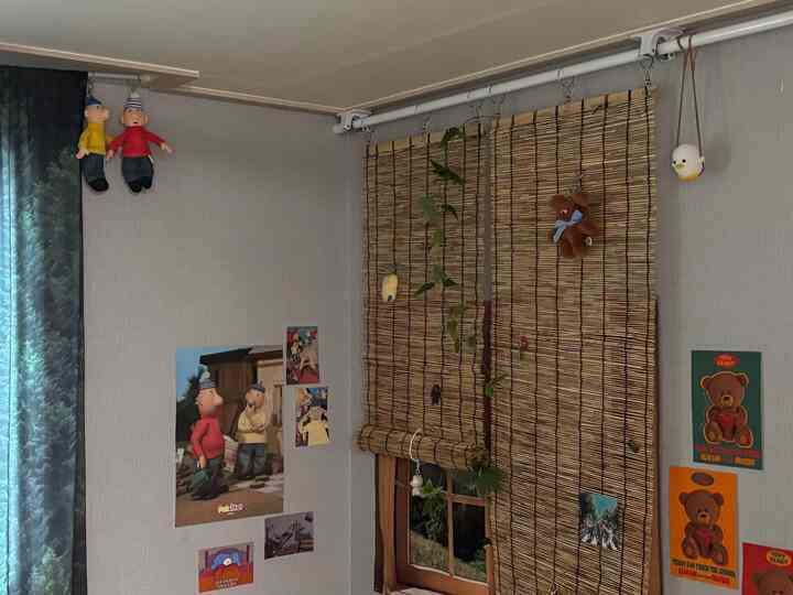 ナチュラルな色調の狭い部屋、竹のロールアップカーテンとポスター、ぬいぐるみが飾られた雰囲気のある壁面インテリア
