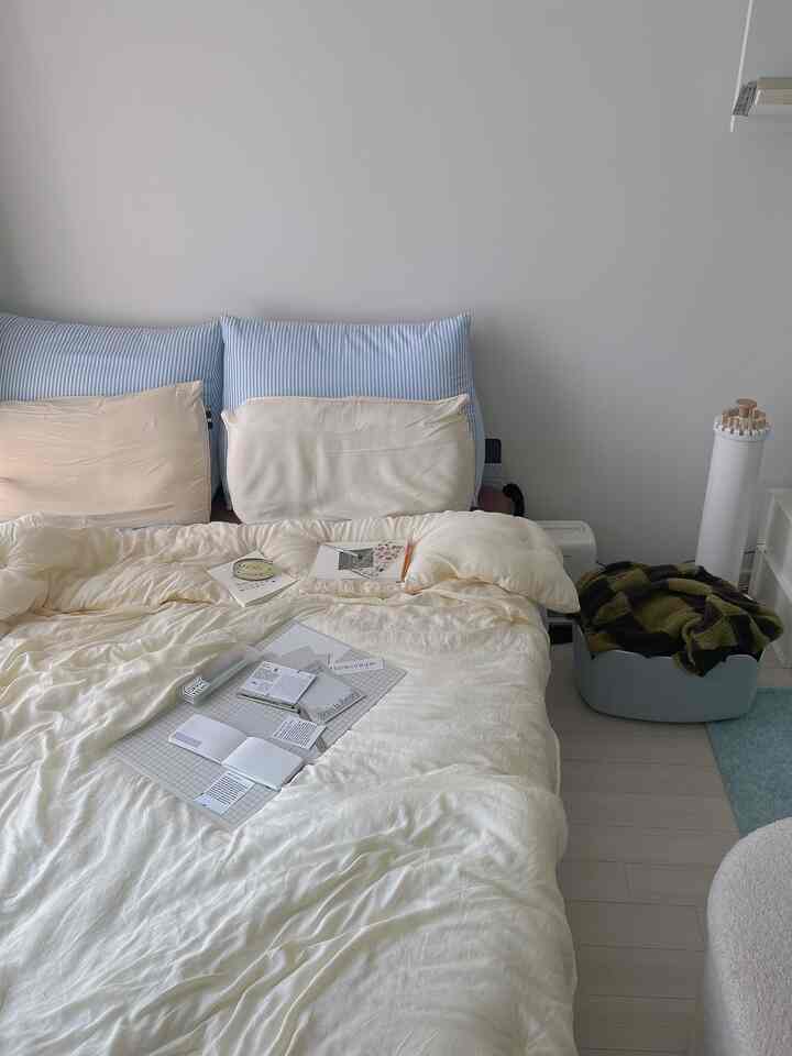 ライトブラウンとホワイトのワンルーム寝室、クリーム色の掛け布団とストライプの枕が温かみのある雰囲気を醸し出す空間