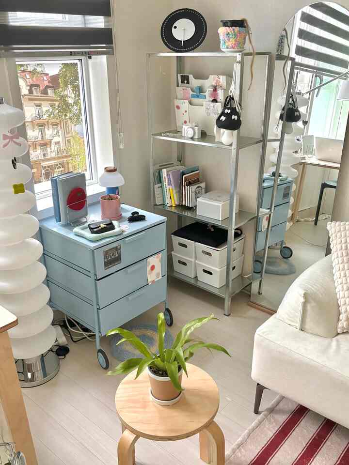 ホワイトとブルーのトーンが調和するコンパクトな一人暮らし用ホームオフィス、収納棚と植物のある木製スツールが配置されたモダンなインテリア