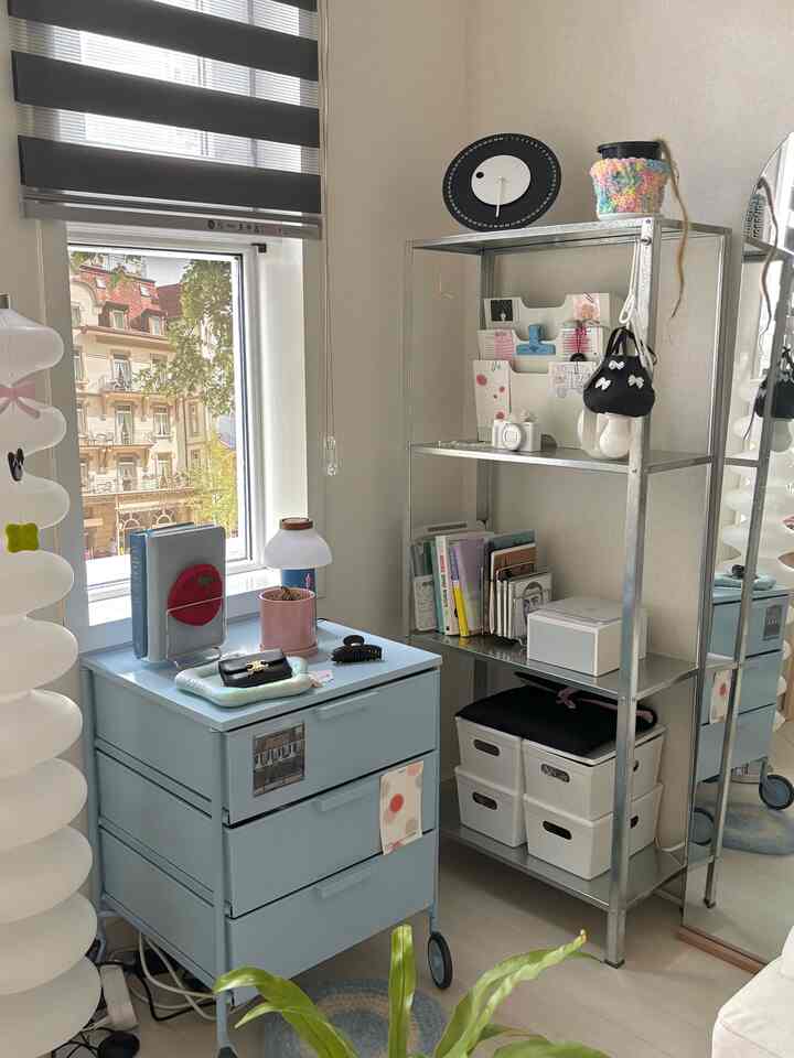 パステル調の収納キャビネットとメタリックグレーの金属製棚が配置されたバルコニー横のかわいらしい収納スペース