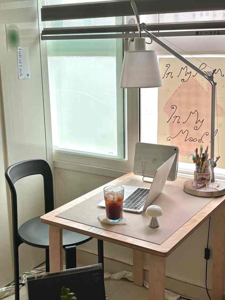 明るい白い壁と木目調のデスクがある小さなホームオフィス、ノートパソコンとテーブルランプが配置された雰囲気のある空間