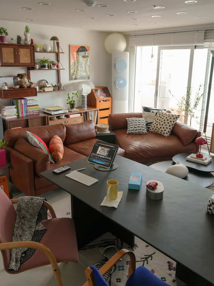 ナチュラルな色調と木製家具が配置されたリビング、茶色のレザーソファと大きな作業用テーブルが印象的な空間