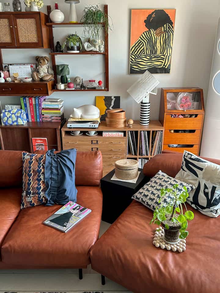 暖かみのあるブラウンレザーソファと木製収納が配置されたナチュラルモダンのリビング、壁にはアートポスターと棚が飾られている。