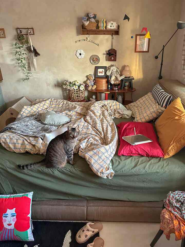 ベージュとグリーンの色調が特徴の寝室、チェック柄の寝具とクッションが配置され、猫が座る自然で落ち着いた雰囲気のインテリア