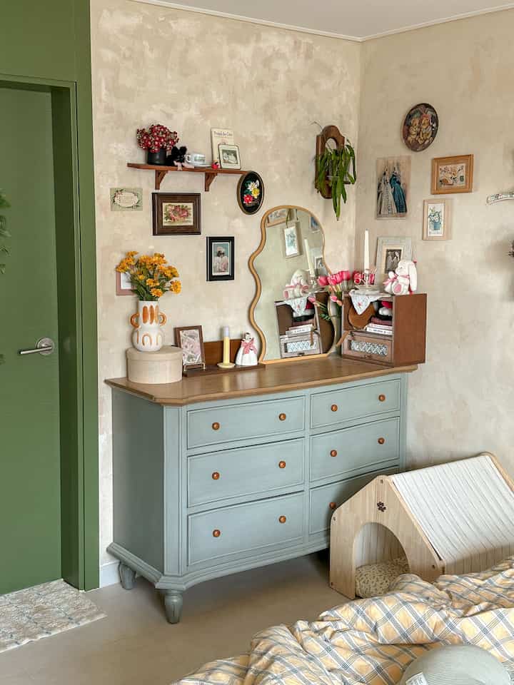 ベージュの壁とパステルブルーのチェストが配された寝室、ヴィンテージ調の鏡とキャットハウスが置かれ、落ち着いた雰囲気のインテリア