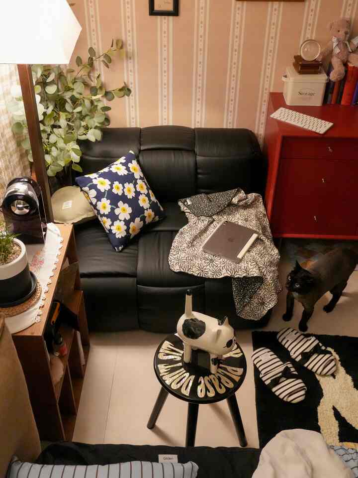 ベージュの壁と黒いレザーソファがある寝室の居心地の良いミニリビングコーナー