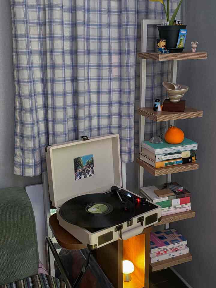 ブルーチェックのカーテンとナチュラルな木製シェルフが配された北欧スタイルの空間で、ターンテーブルとサイドテーブルが並ぶ落ち着いた雰囲気のインテリア