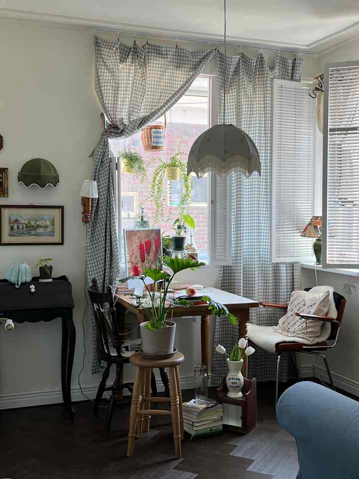 青と白の柄のカーテンがあるコーナーリビング、ナチュラルな木製デスクと椅子、植物のある雰囲気のあるインテリア