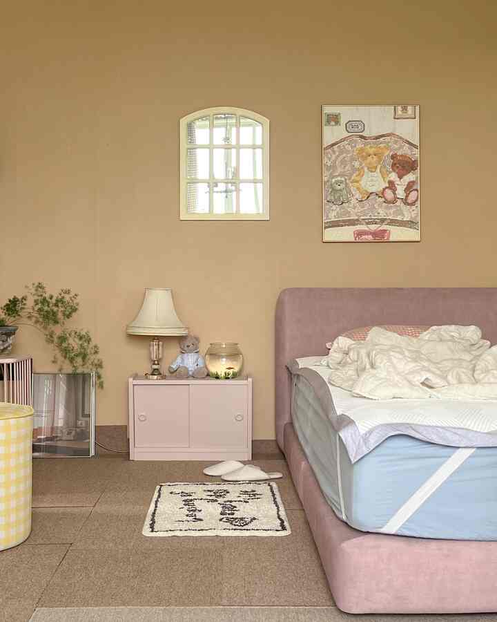 ピンクのベッドフレームとベージュの壁が調和した、小さくて居心地の良い子供部屋、ぬいぐるみやかわいらしい小物が配置された空間