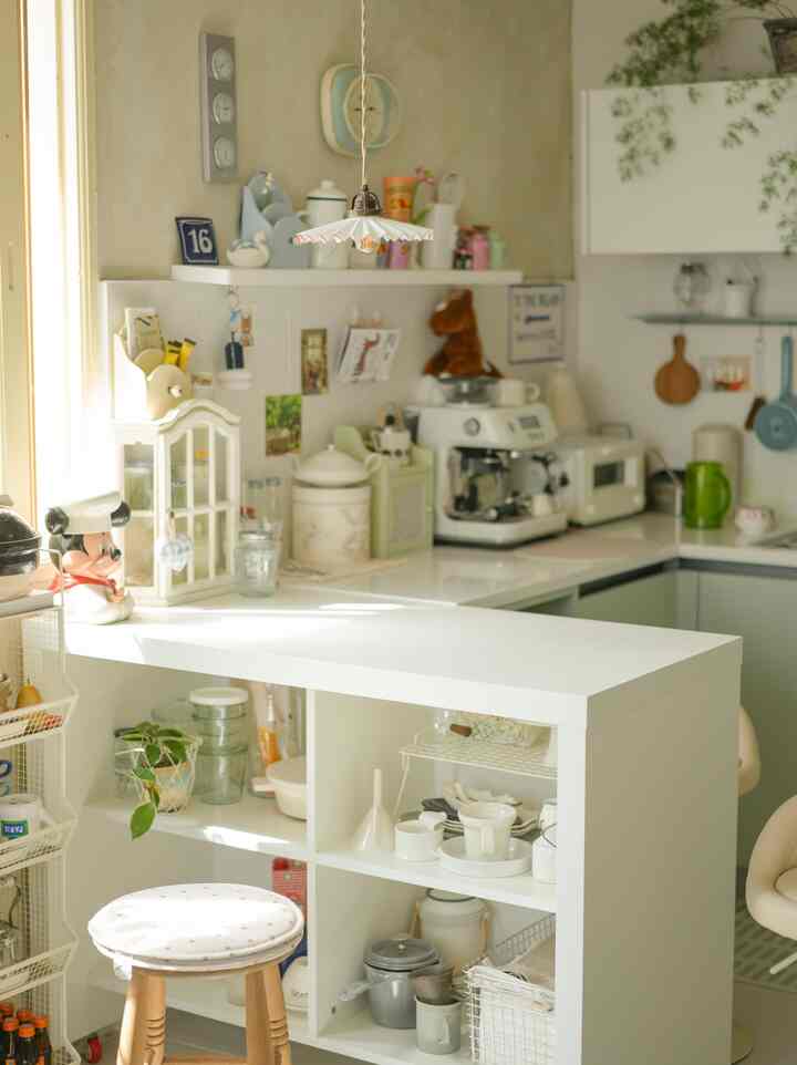 明るいホワイトとグリーンの色調のキッチン、キッチンアイランドとエスプレッソマシン、木製スツールが配置された自然な雰囲気のホームカフェ