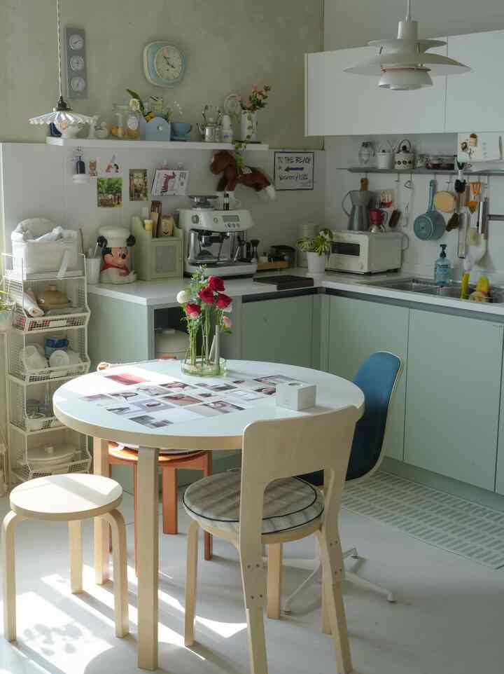 ミント色の下部収納とホワイトの上部収納があるキッチン空間、円形のダイニングテーブルと様々な椅子が配置された雰囲気のあるインテリア