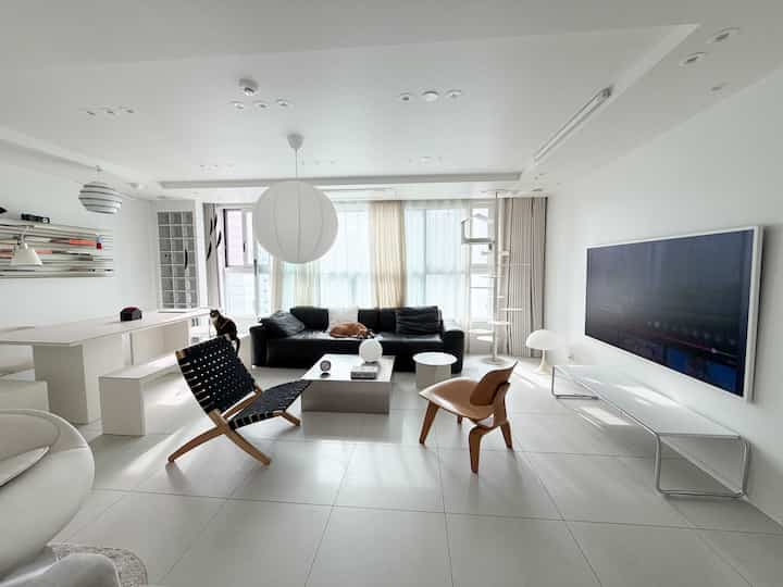 ホワイトのモダンなリビング、黒いソファとキャットタワー、大型テレビが配置された明るく清潔な空間