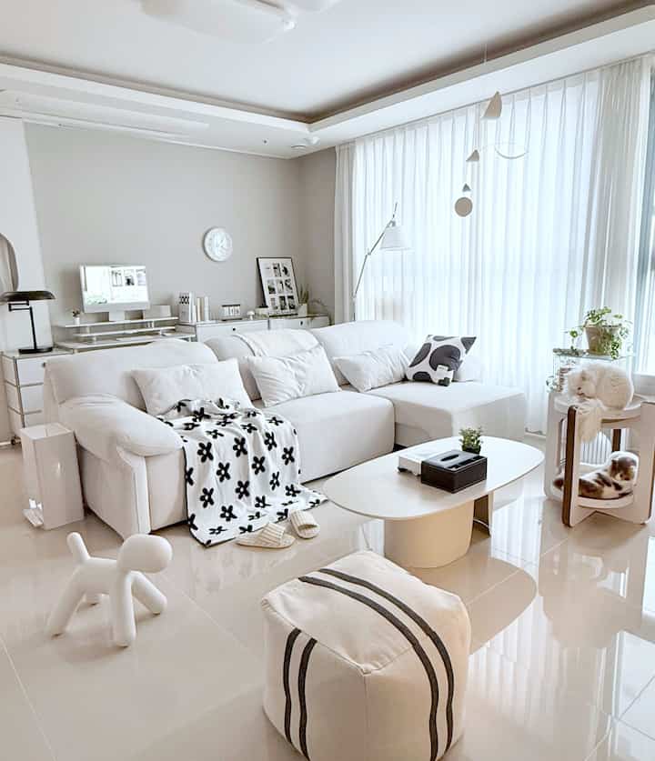 明るいモノトーンのナチュラルモダンなリビング、中央に白い大きなソファとコーヒーテーブル、右側にキャットタワーと猫が見える空間